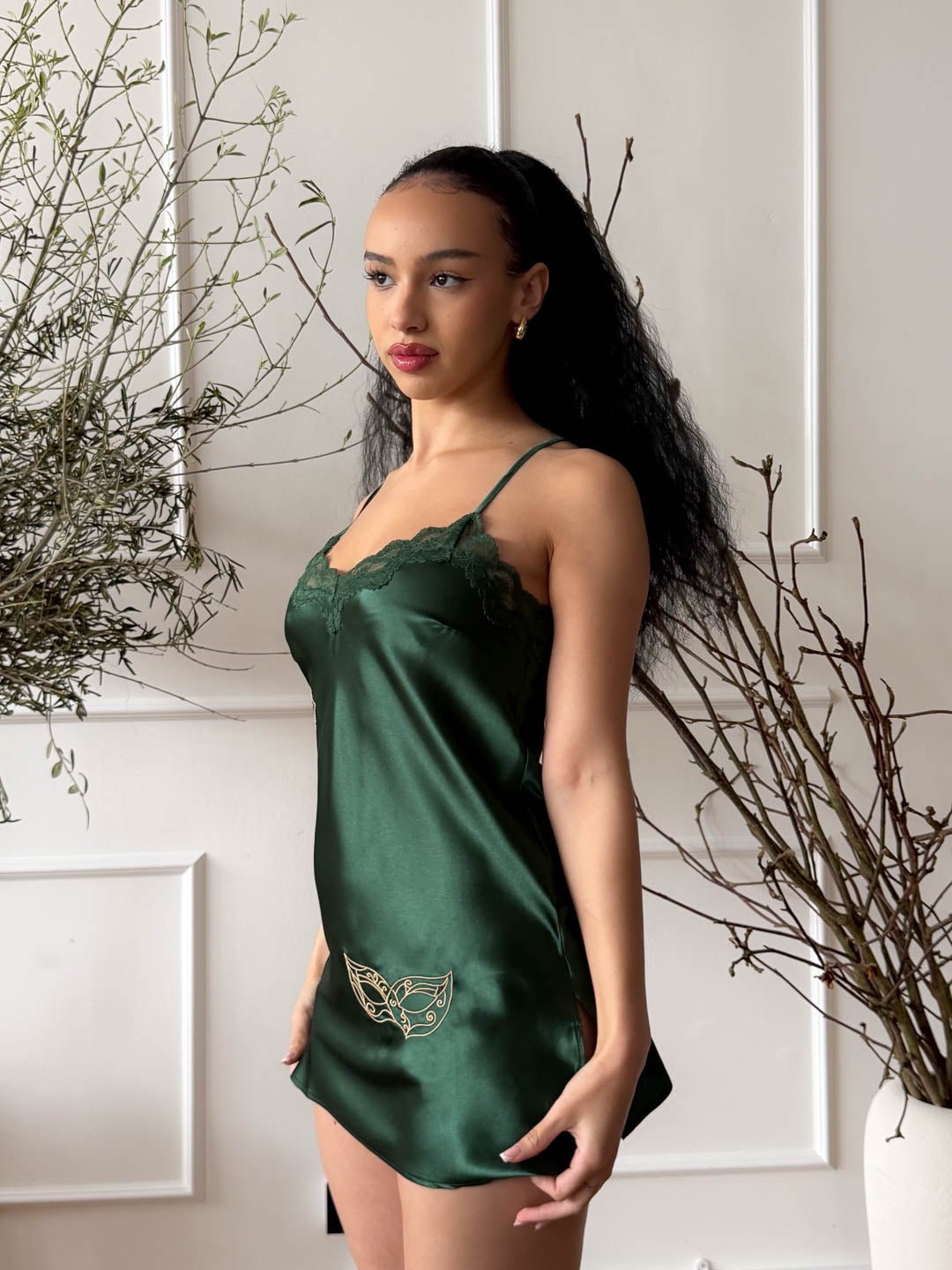 Side view of a model wearing an emerald green satin mini chemise with elegant gold mask embroidery inspired by Brazilian carnival spirit.