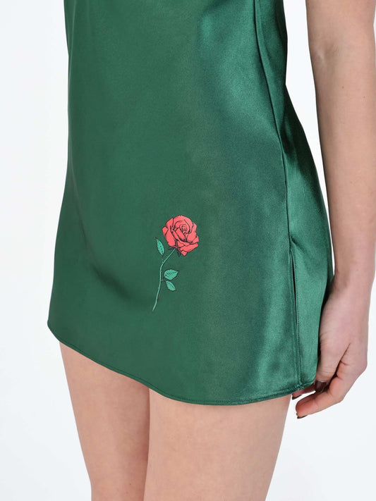 Close-up of a rose print detail on an emerald green satin chemise worn by a model.